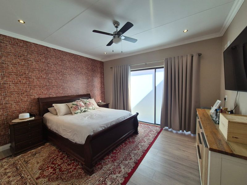A well-maintained bedroom featuring a brick-effect accent wall, recessed lighting, a ceiling fan, and a sliding glass door providing natural light.