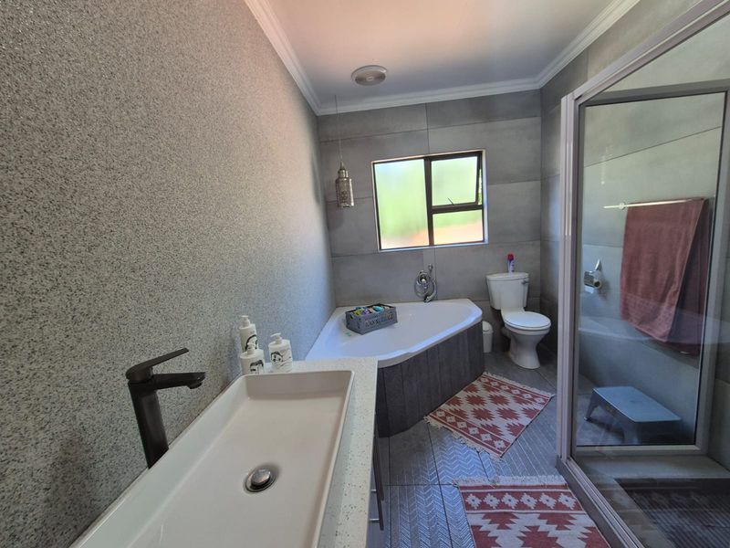 Modern bathroom featuring a corner bathtub, separate glass shower enclosure, vessel sink with contemporary faucet, and neutral tiled finishes.