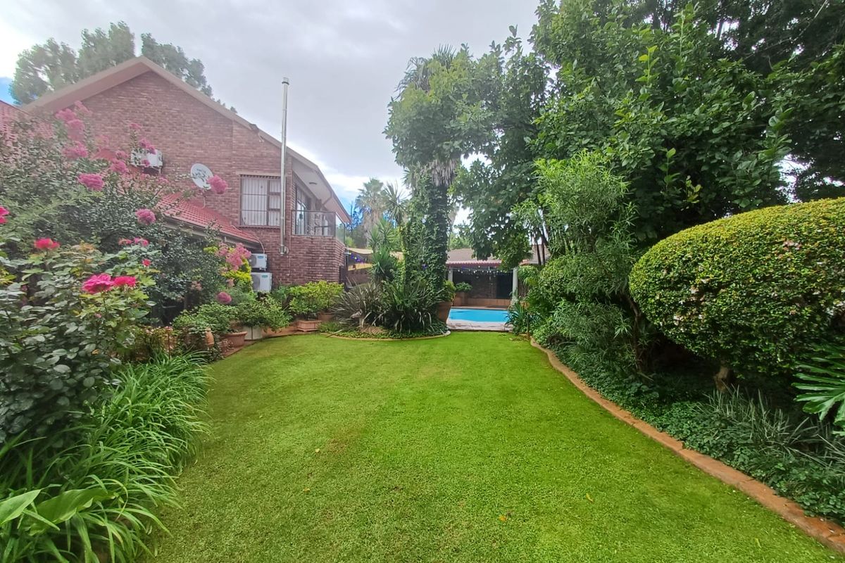 A well-maintained rear garden featuring a lush green lawn, mature landscaping, and a swimming pool visible in the background.