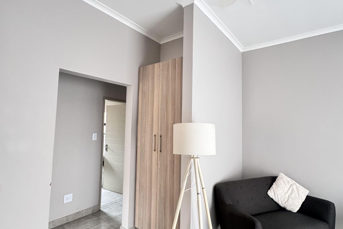 A bedroom featuring neutral grey walls, tiled flooring, and a built-in wooden cupboard, with a visible water stain on the ceiling.