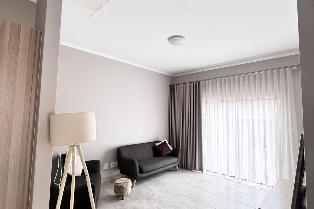A living room featuring tiled flooring, neutral wall tones, and large sliding doors with curtains leading to an outdoor area.