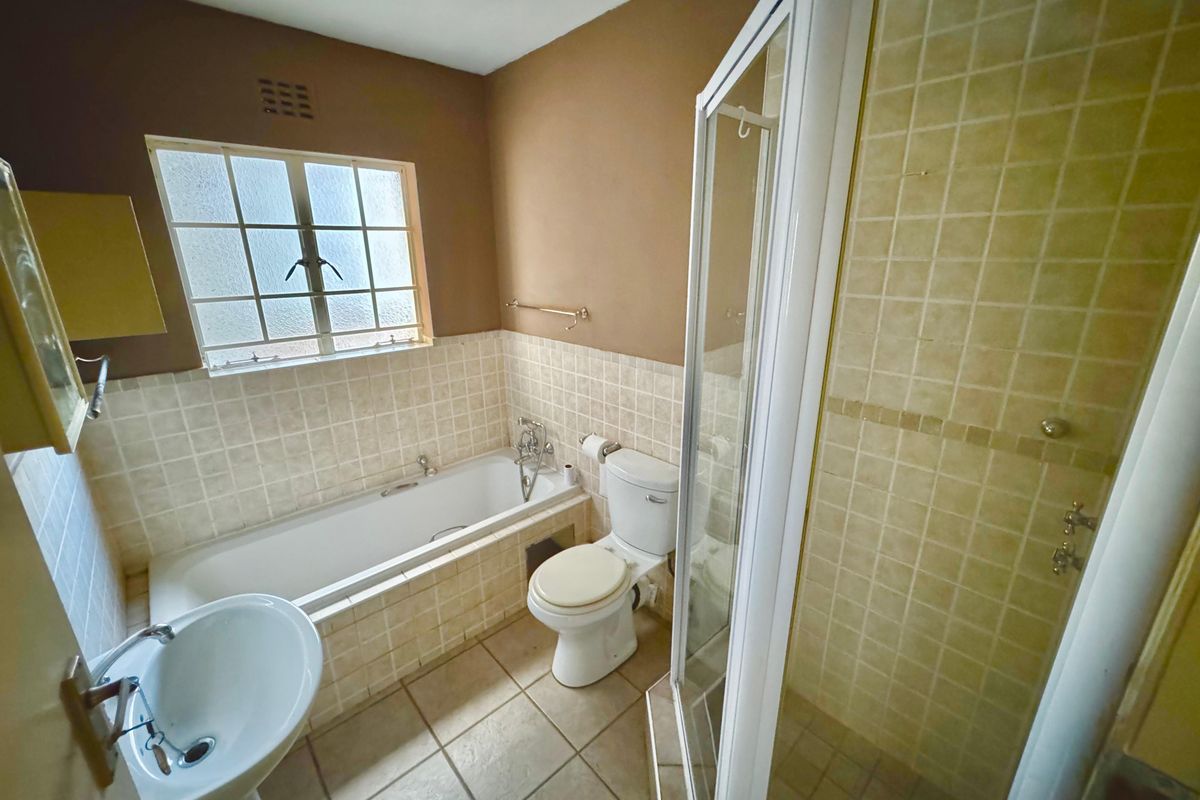 A functional bathroom featuring a separate bathtub and shower enclosure, pedestal basin, and toilet with neutral tiled finishes.