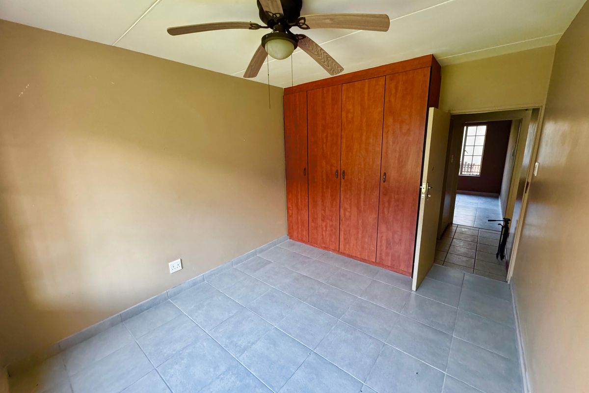 A vacant bedroom featuring neutral walls, tiled flooring, a ceiling fan, and built-in wooden cupboards.