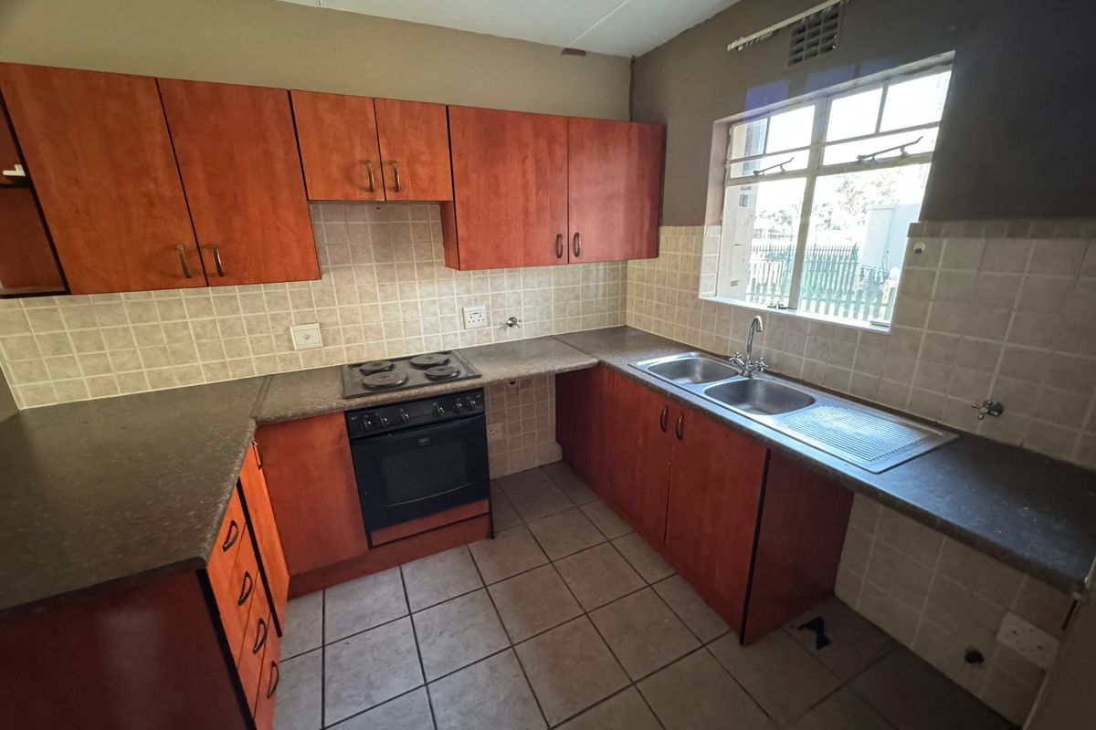 A functional kitchen featuring wooden cabinetry, laminate countertops, a built-in electric stove and oven, and a double basin sink with tiled backsplash.