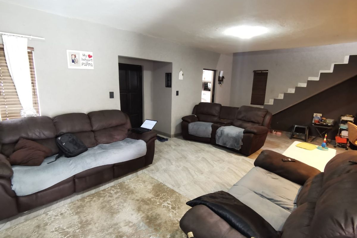 Spacious open-plan living area featuring tiled flooring, a staircase, and neutral wall tones, providing a functional layout for family living.