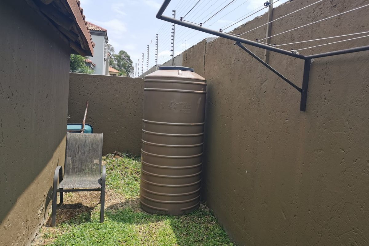 Side exterior area featuring a water storage tank, wall-mounted washing line, and perimeter boundary wall with electric fencing.