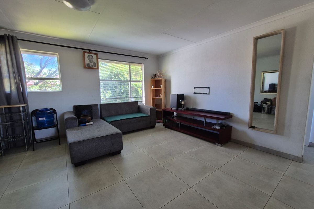 A spacious living room featuring large ceramic floor tiles, natural light from dual windows, and a neutral wall finish.