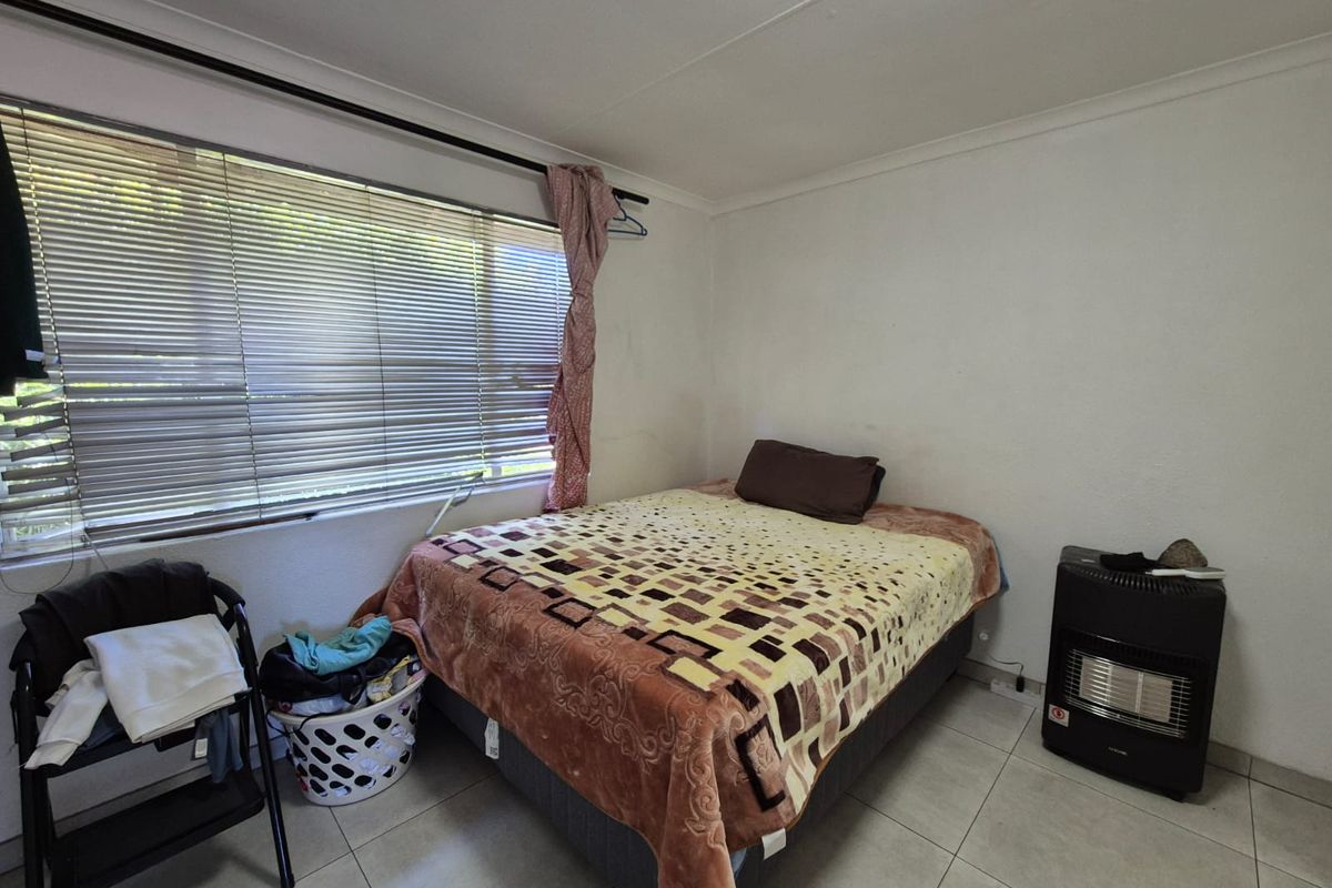 A functional bedroom featuring tiled flooring and a large window with fitted blinds, providing natural light.