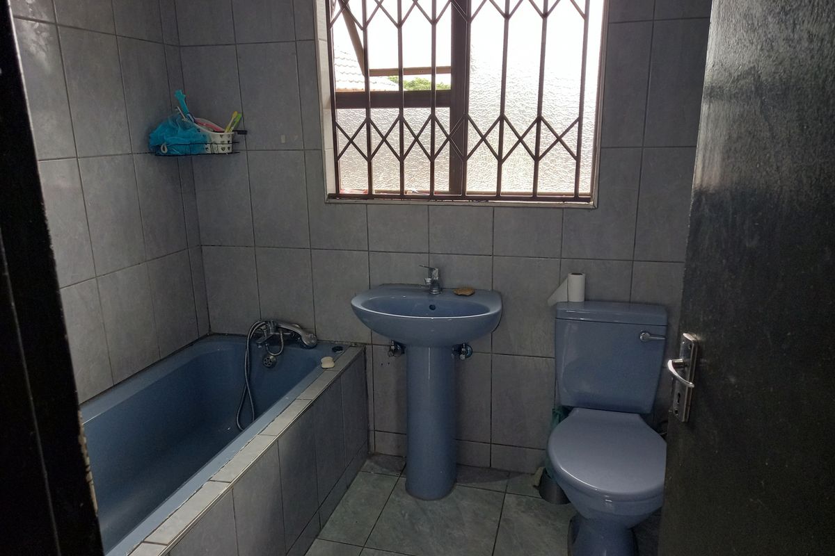 A functional bathroom featuring a blue pedestal basin, matching toilet, and a built-in bathtub with tiled surround and security bars on the window.