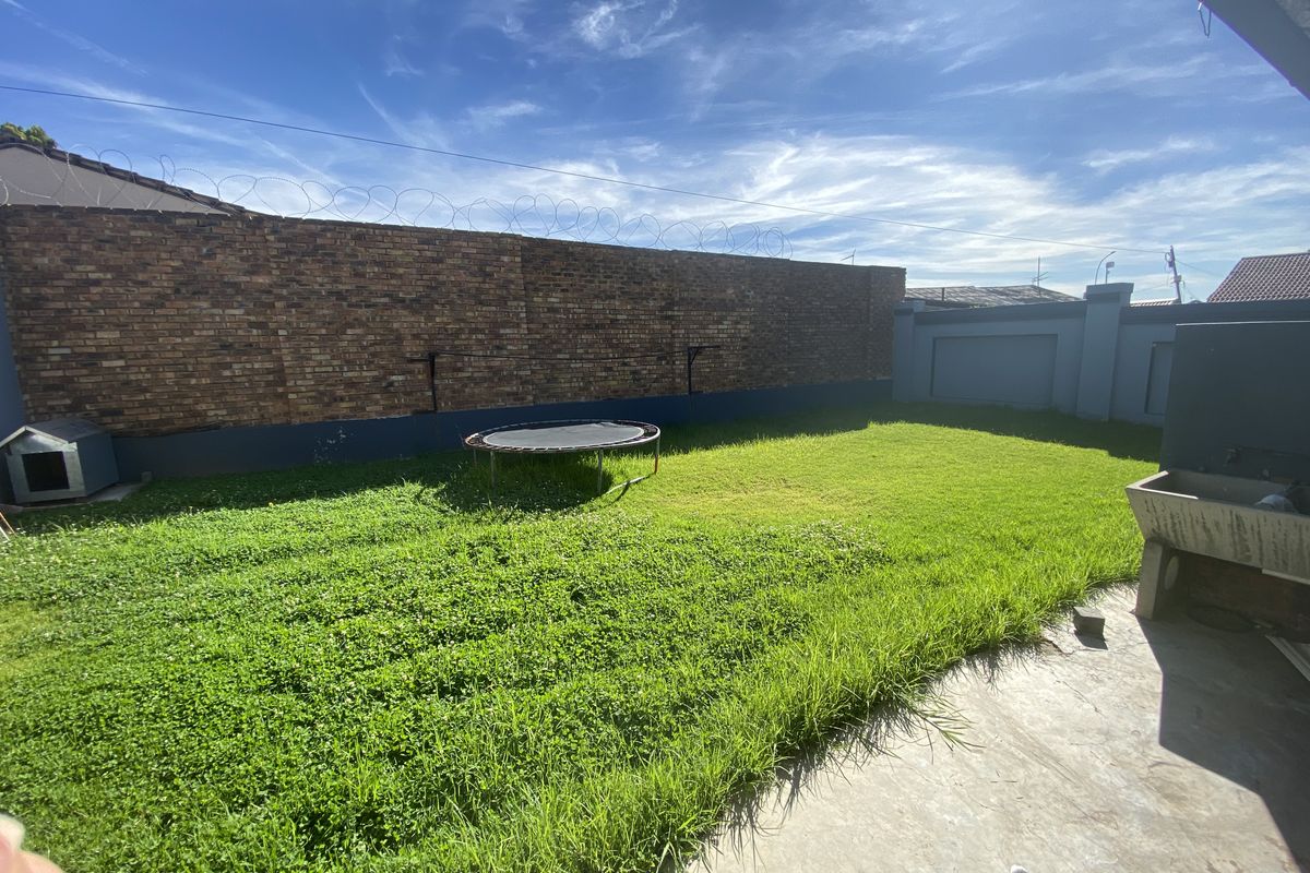 A private rear garden featuring a lawn area, concrete patio, and high perimeter brick walls with security fencing.