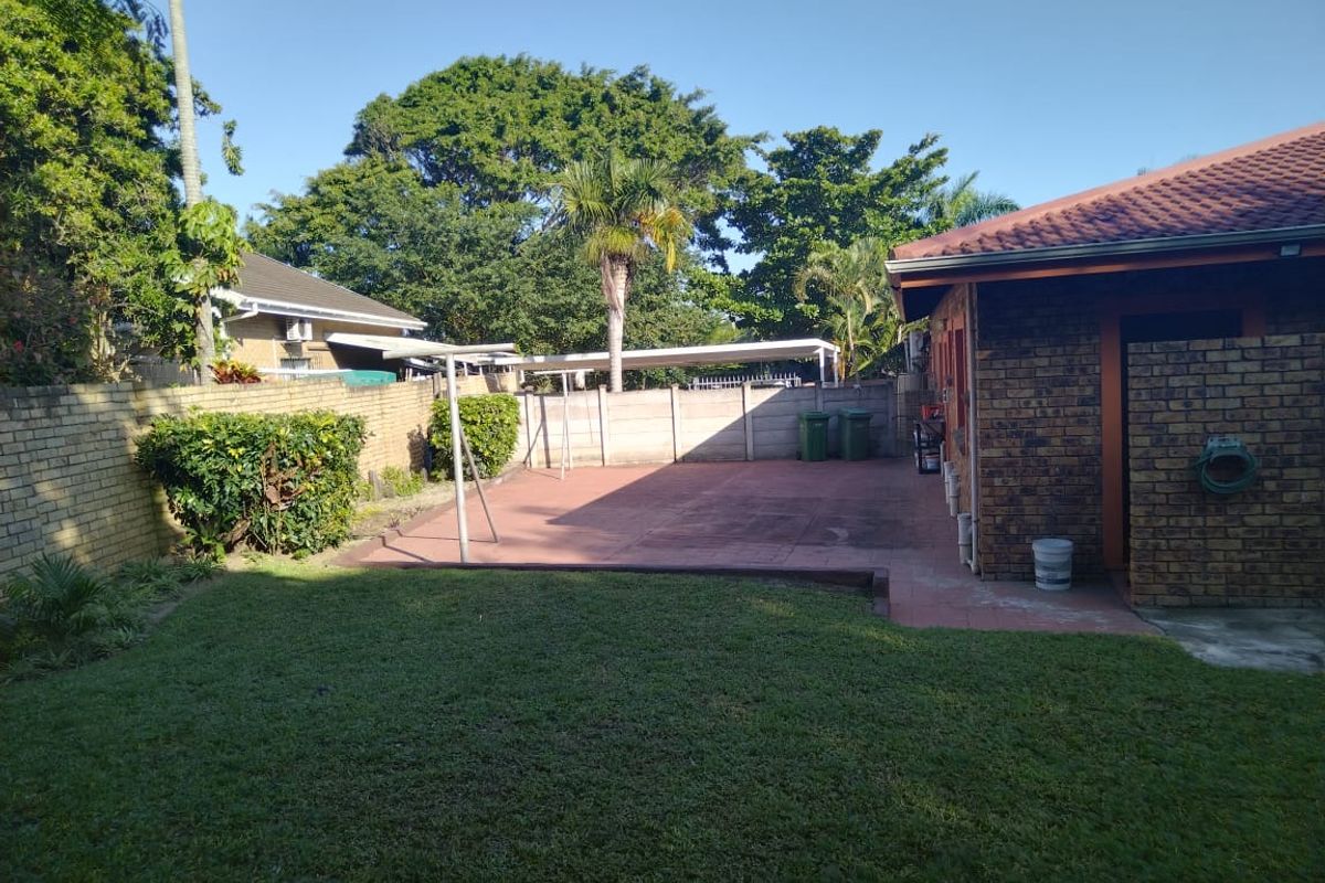 A private rear garden featuring a paved patio area, established lawn, and perimeter boundary walling, providing a functional outdoor space.