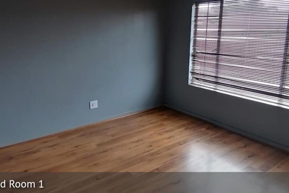 A bedroom featuring laminate wood flooring, grey painted walls, and fitted venetian blinds.