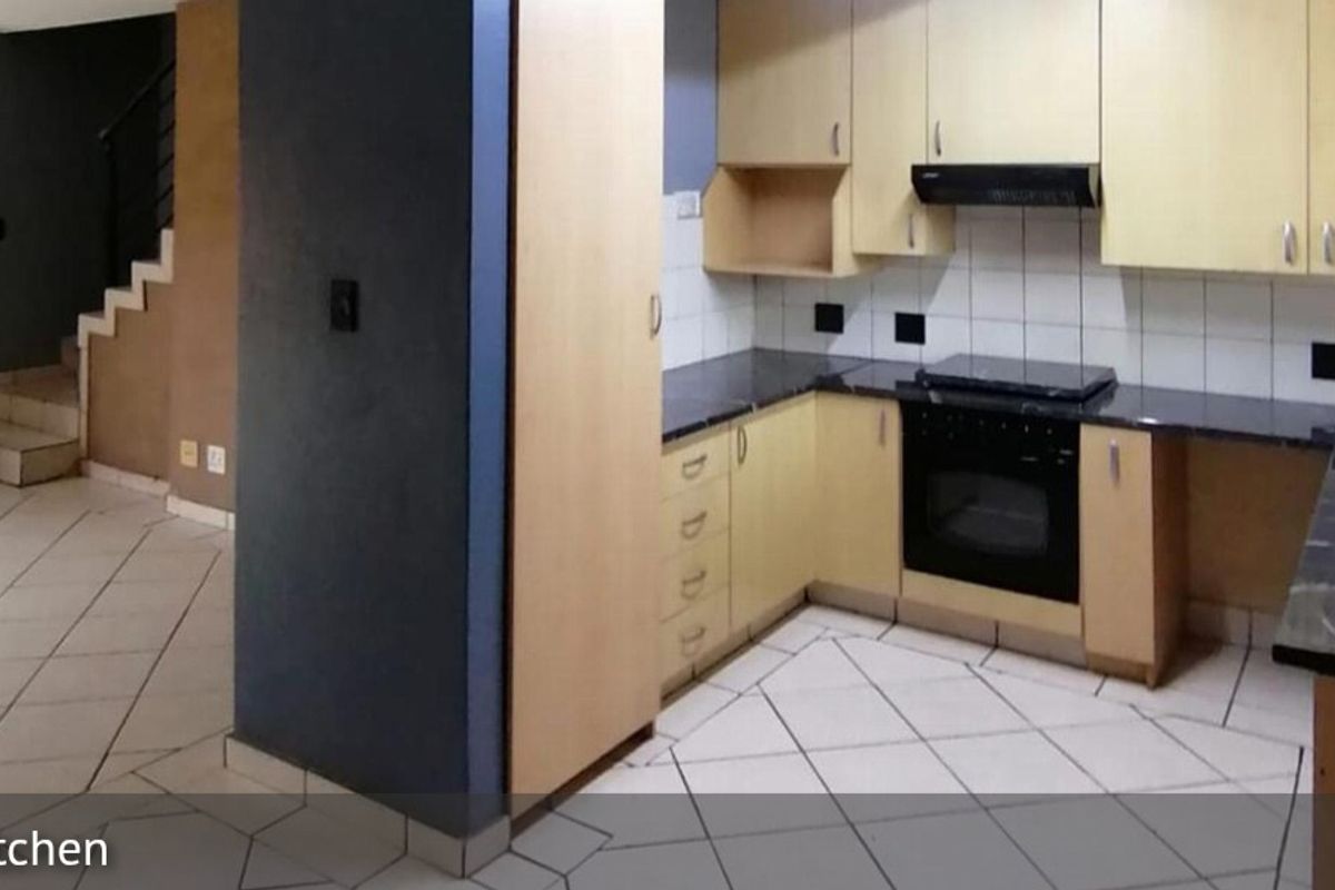 A functional kitchen featuring light wood cabinetry, dark countertops, and a built-in oven with extractor fan, adjacent to an open-plan living area.