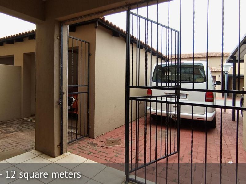 A covered patio area featuring paved flooring and a security gate, providing a functional outdoor space for the townhouse.