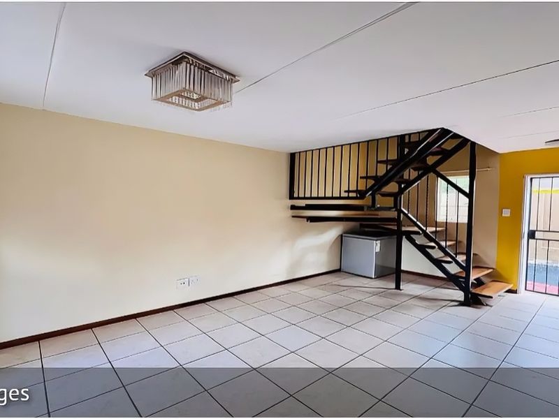 An open-plan living area featuring tiled flooring and a prominent metal staircase leading to the upper level, with direct access to an outdoor space.
