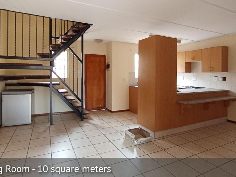 Open plan living and kitchen area featuring tiled flooring, a metal staircase, and built-in cabinetry with a breakfast bar.