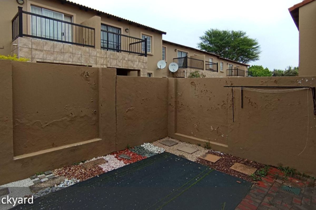 A private rear courtyard featuring a paved area, pebble landscaping, and a wall-mounted washing line, enclosed by a boundary wall requiring maintenance.