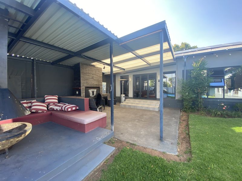 Spacious covered patio featuring a built-in braai with stone cladding, concrete flooring, and direct access to the home through sliding doors.