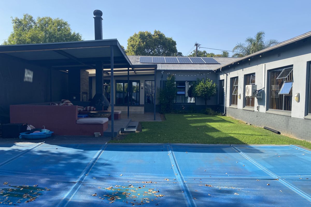 Rear exterior view featuring a swimming pool with cover, a covered patio area with an outdoor fireplace, and solar panels on the roof.