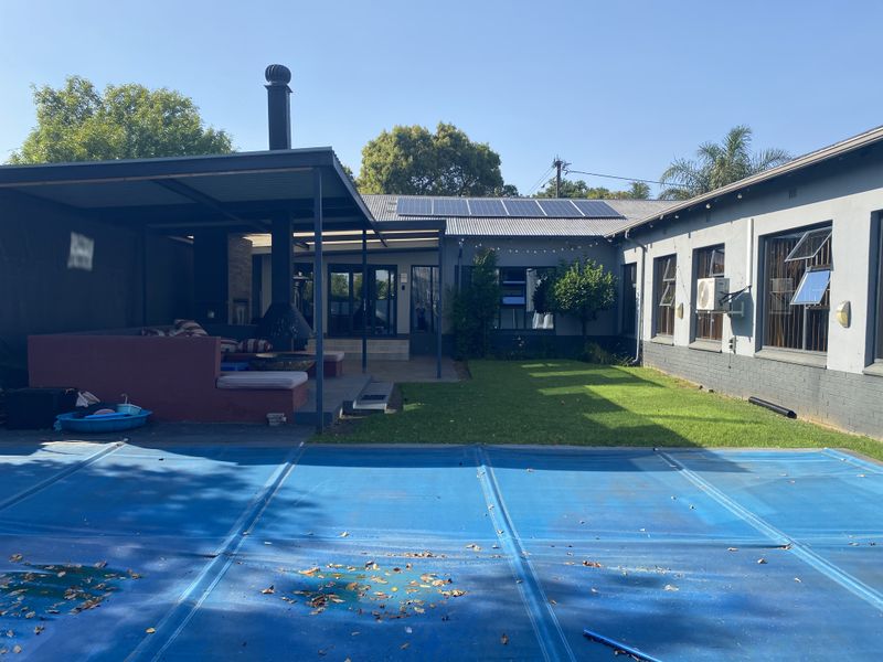 Rear exterior view featuring a swimming pool with cover, a covered patio area with an outdoor fireplace, and solar panels on the roof.