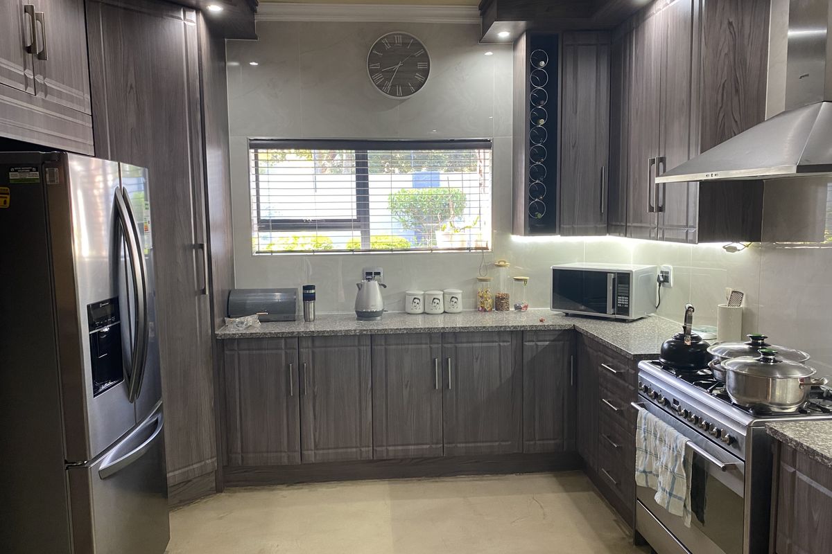 Modern kitchen featuring dark wood-grain cabinetry, granite countertops, stainless steel appliances, and integrated lighting, offering a functional and contemporary cooking space.