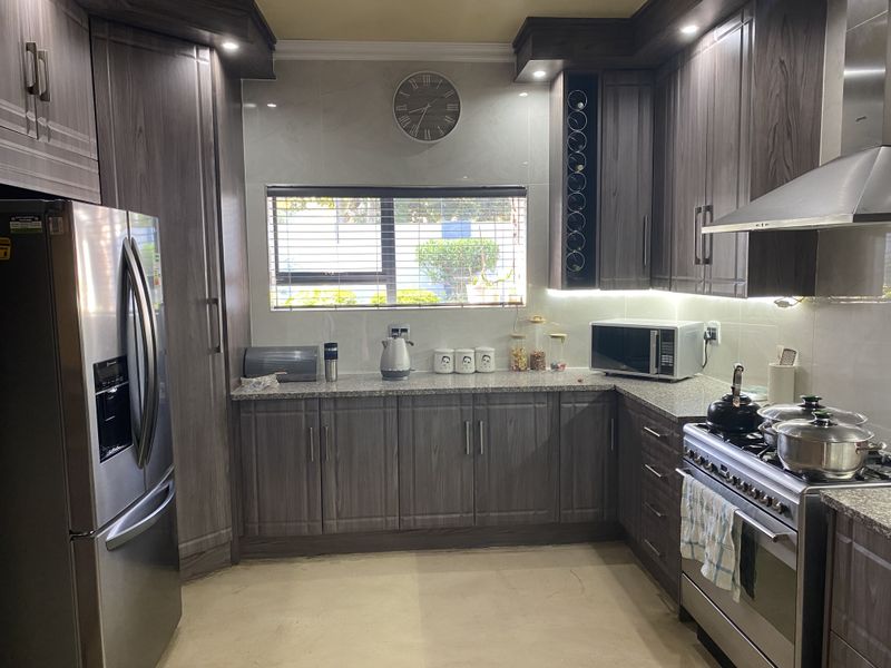 Modern kitchen featuring dark wood-grain cabinetry, granite countertops, stainless steel appliances, and integrated lighting, offering a functional and contemporary cooking space.
