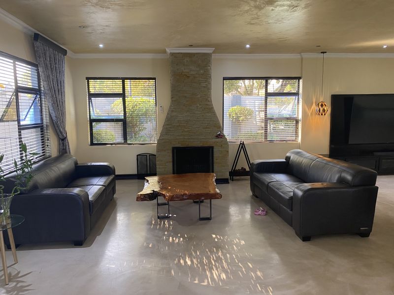 Spacious living room featuring a prominent stone-clad fireplace, polished concrete floors, and large windows with venetian blinds providing ample natural light.