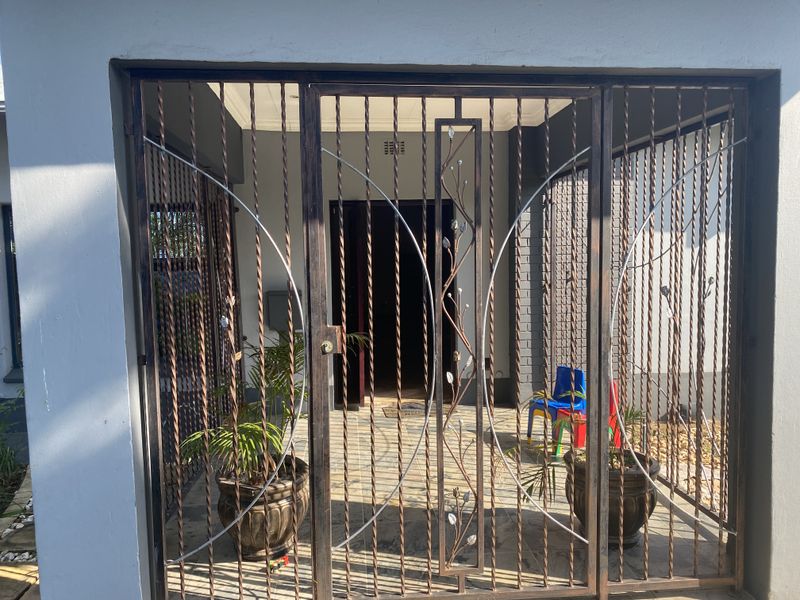 A secure entrance area featuring a decorative metal security gate leading to a covered porch and the main front door.