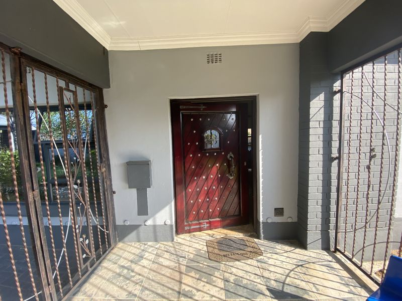 A covered entrance porch featuring a solid wood front door, tiled flooring, and secure metal gates.