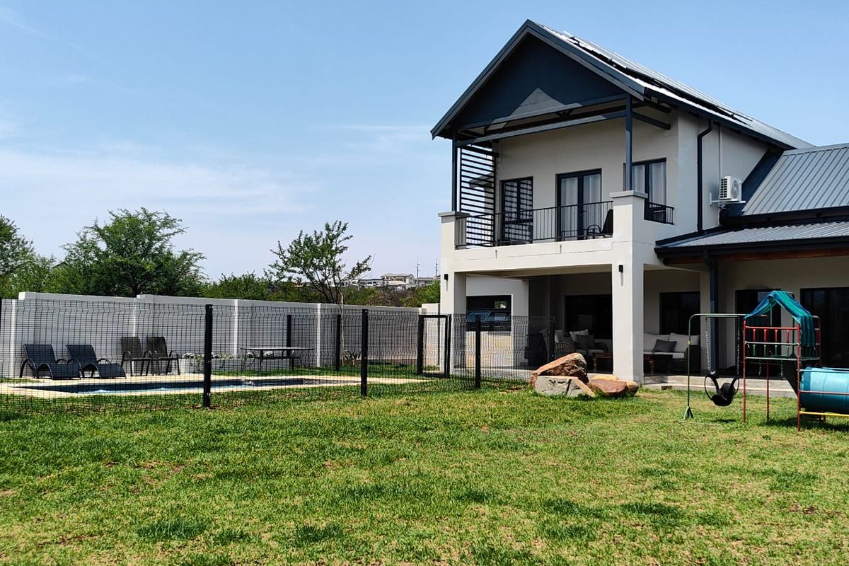 Rear view of a two-story house featuring a swimming pool, fenced garden area, and an upper-level balcony with metal railings.