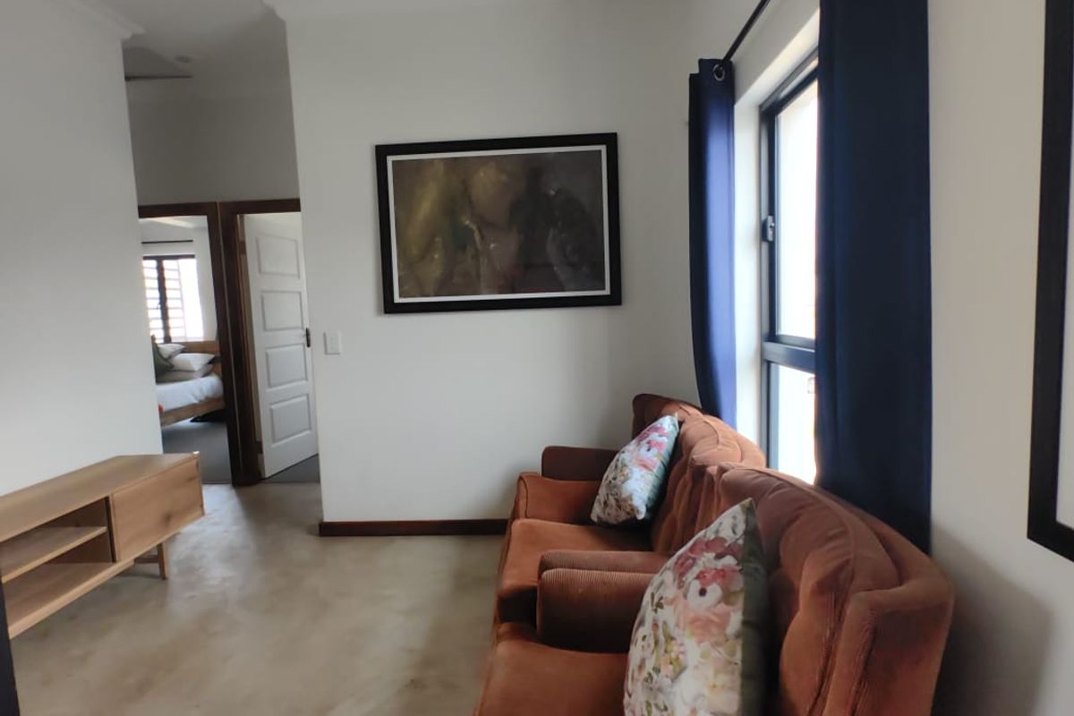 A living room featuring polished concrete flooring, large windows with dark curtains, and a view into an adjacent bedroom.