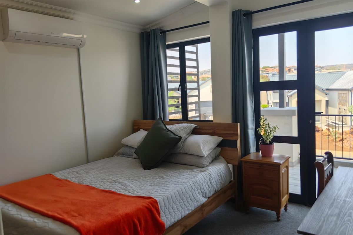 A well-lit bedroom featuring a wall-mounted air conditioning unit, large windows, and direct access to a balcony area.
