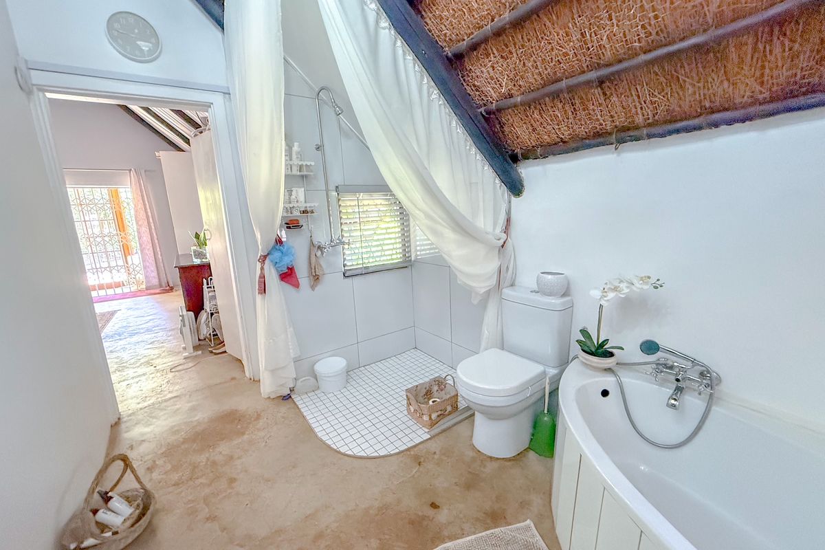 A rustic bathroom featuring a corner bathtub, a walk-in shower area with tiled flooring, and a toilet, set under a traditional thatched roof.
