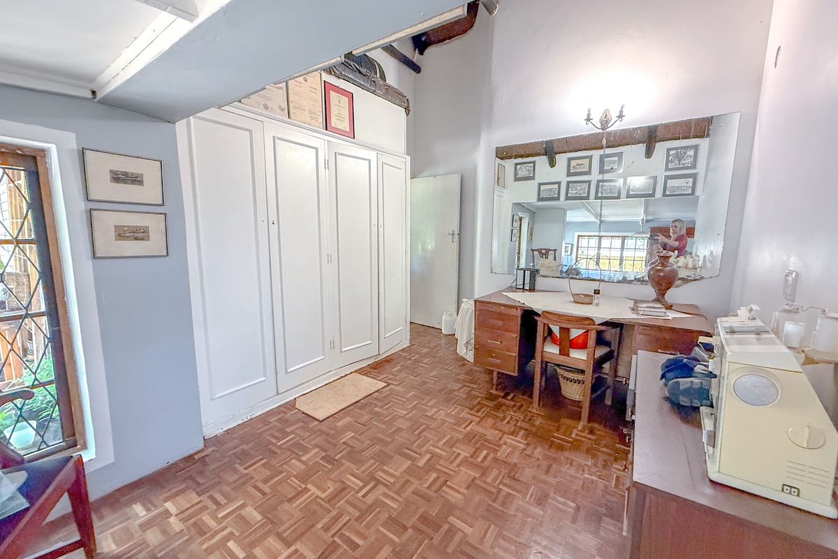 A bedroom featuring built-in white cabinetry, parquet flooring, and a large wall-mounted mirror, offering a classic aesthetic with potential for modernization.