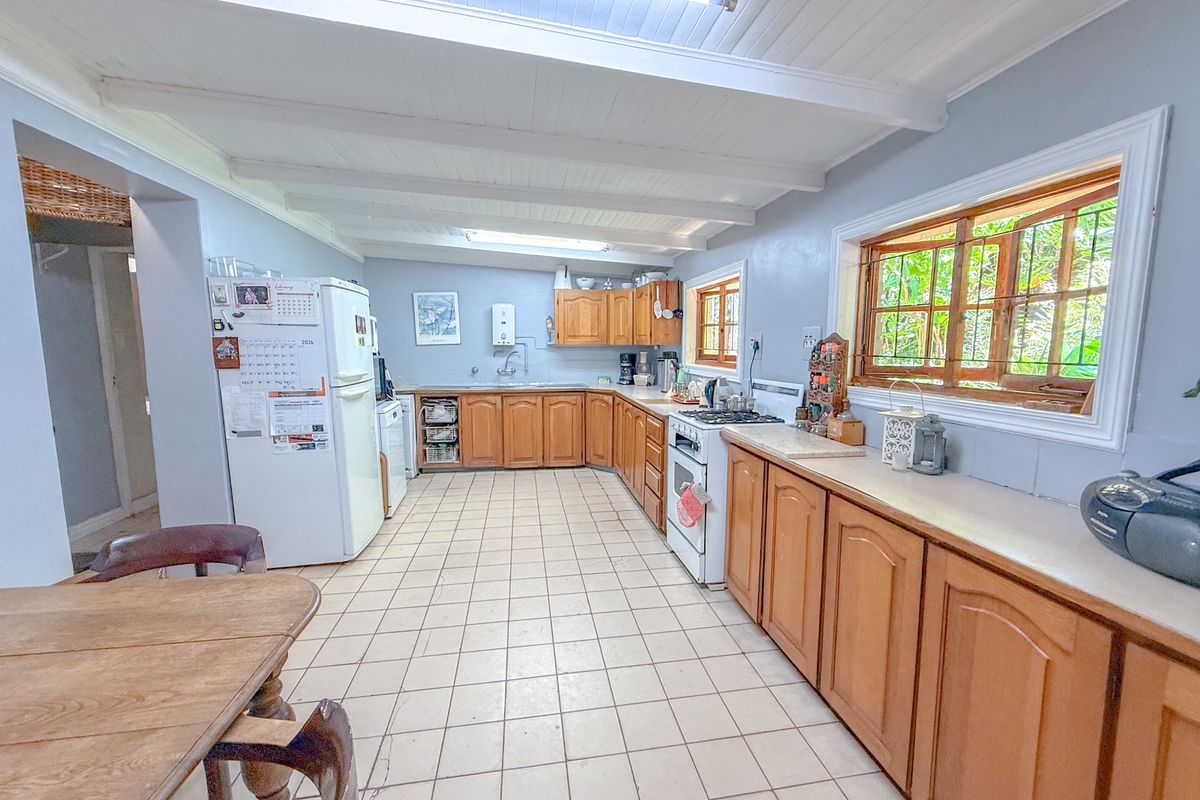 Spacious kitchen featuring wooden cabinetry, tiled flooring, exposed beam ceiling, and large windows providing natural light.