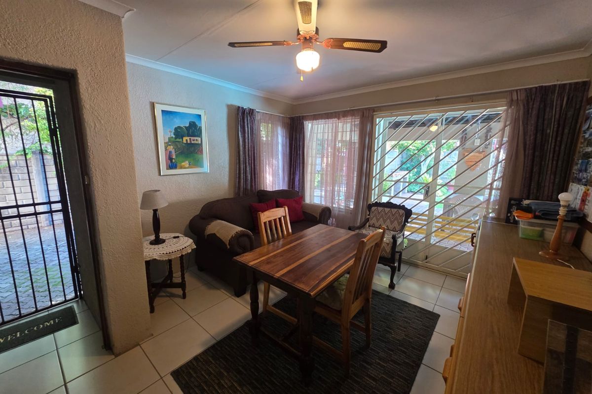 A functional living and dining area featuring tiled flooring, a ceiling fan, and sliding glass doors with security gates leading to the outdoor space.