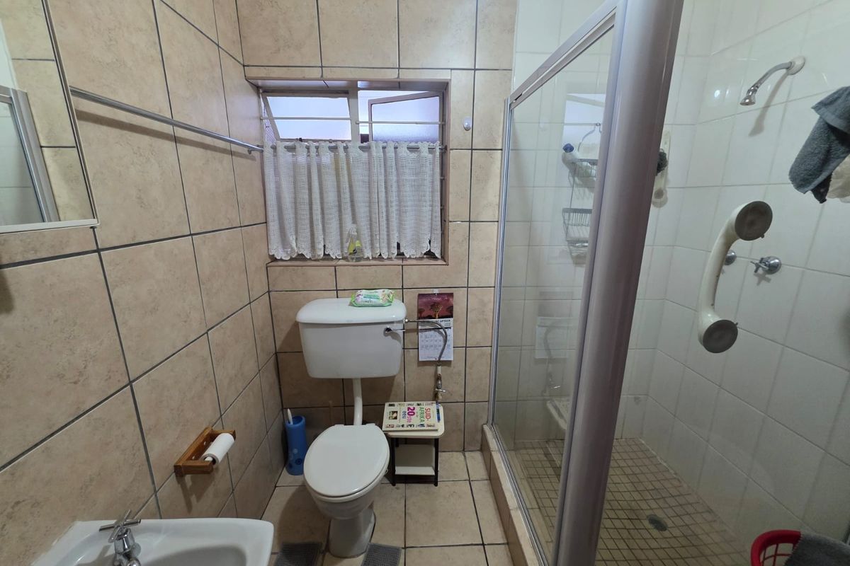 A functional bathroom featuring a glass-enclosed shower, ceramic wall and floor tiles, a standard toilet, and a wall-mounted basin.
