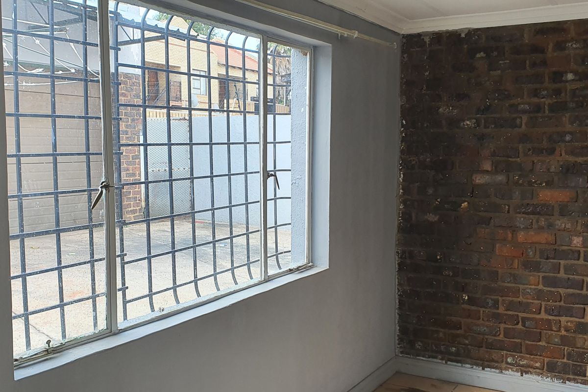 An interior room featuring an exposed brick feature wall, large window with security bars, and neutral painted walls.