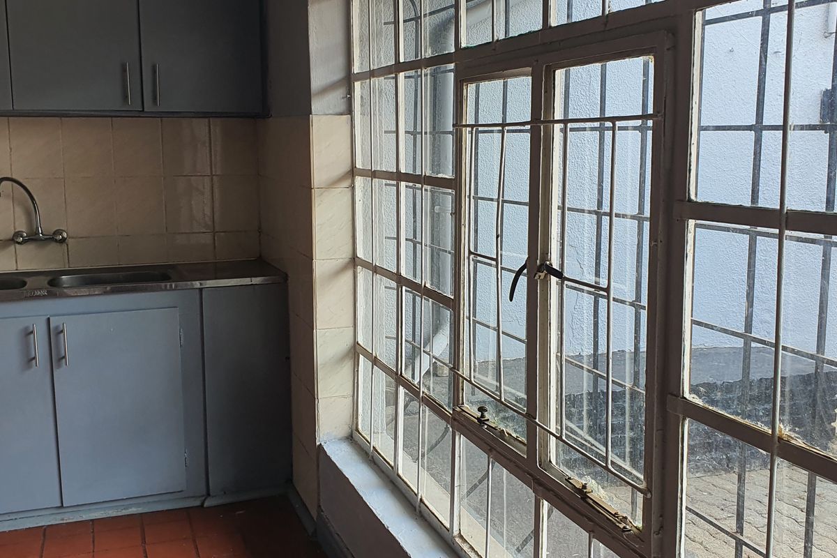 A functional kitchen area featuring built-in cabinetry, a stainless steel sink, and large windows with security bars overlooking the exterior.