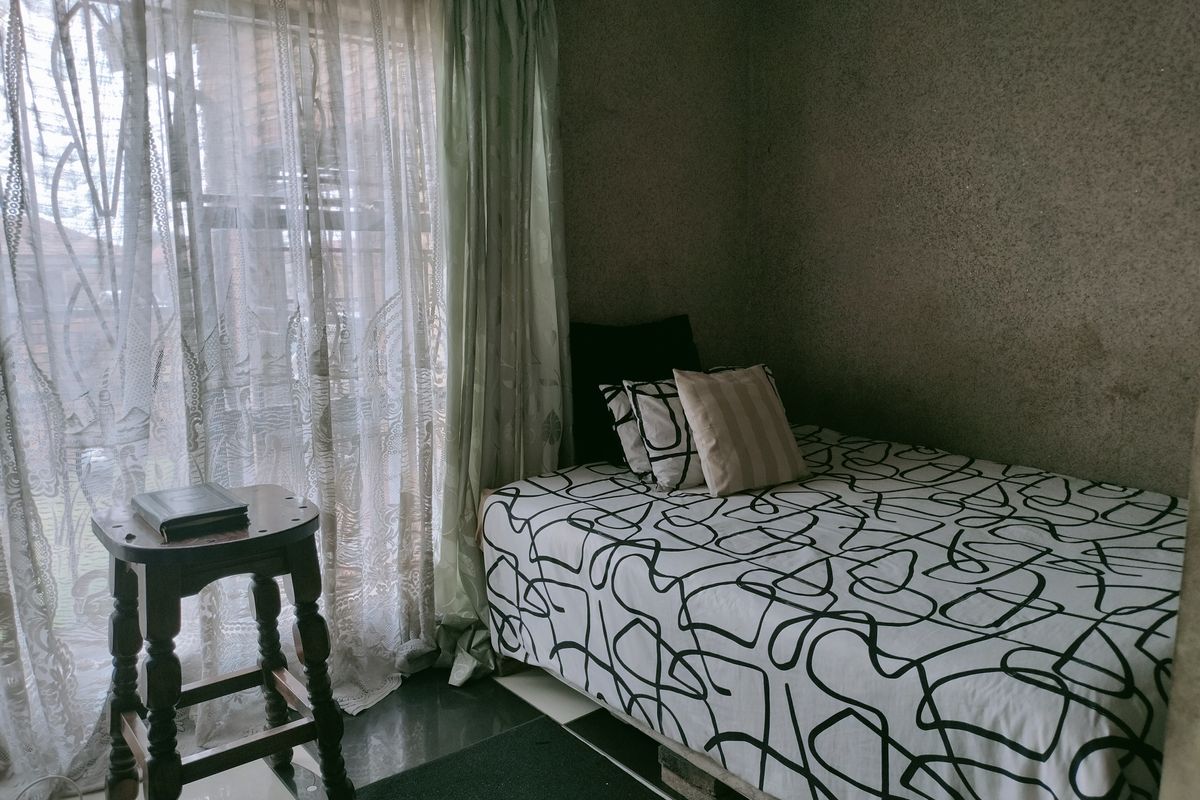 A compact bedroom featuring textured wall finishes, tiled flooring, and a large window with curtain treatments.