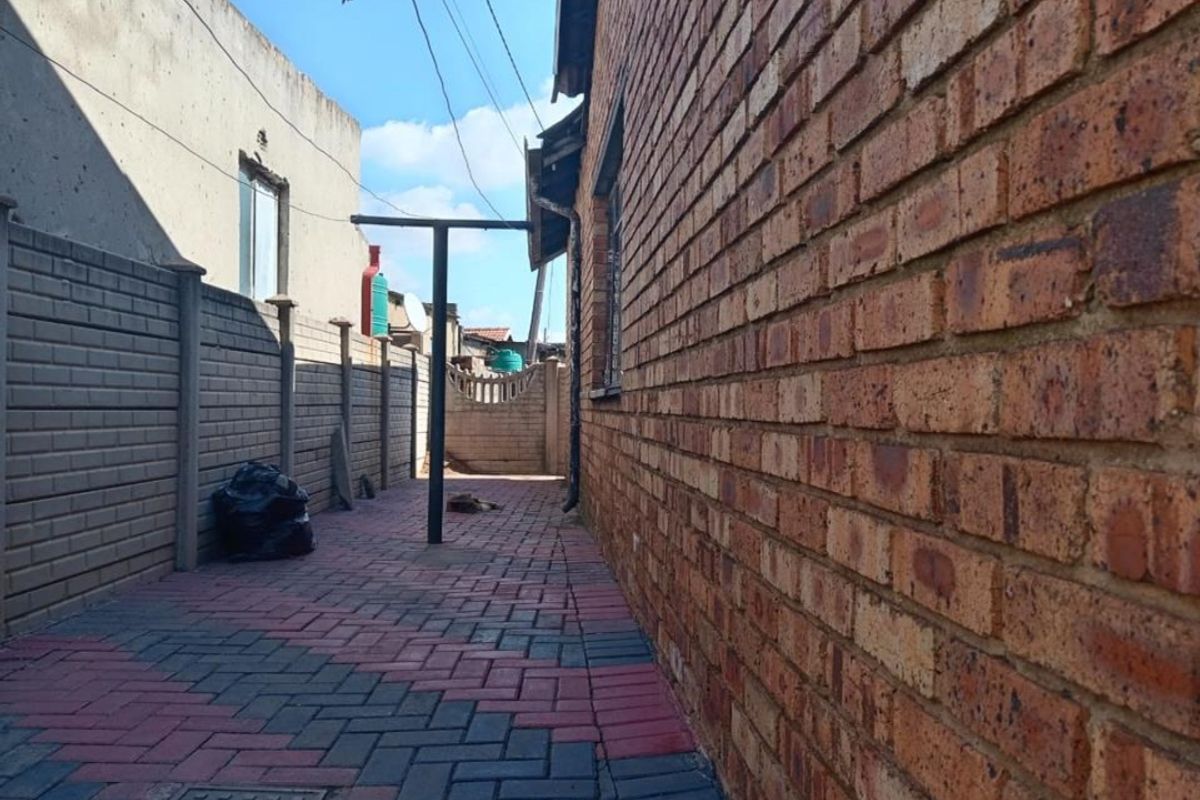 A side exterior walkway featuring red and grey paved flooring, enclosed by a brick wall and a precast concrete boundary wall.