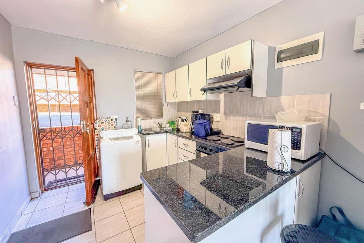 Compact kitchen featuring granite countertops, built-in cabinetry, an integrated extractor fan, and direct access to an exterior door.