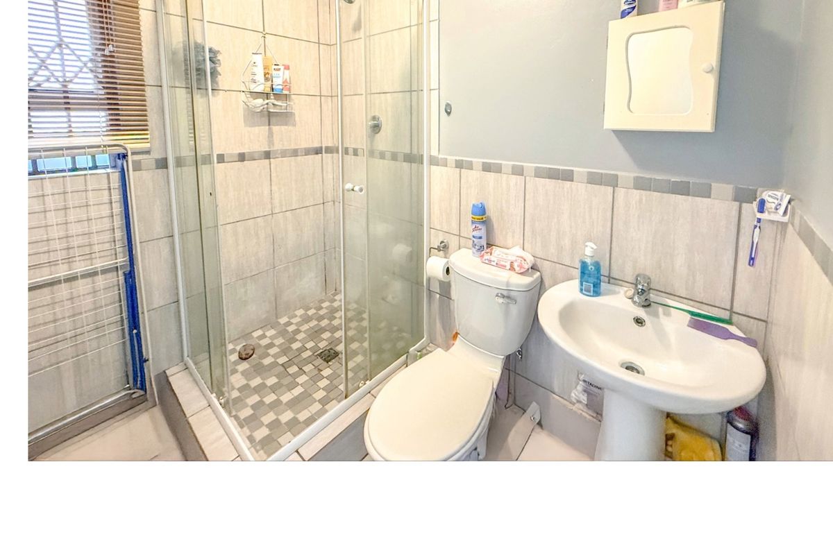A functional bathroom featuring a glass-enclosed shower, pedestal sink, and toilet, finished with neutral wall and floor tiling.