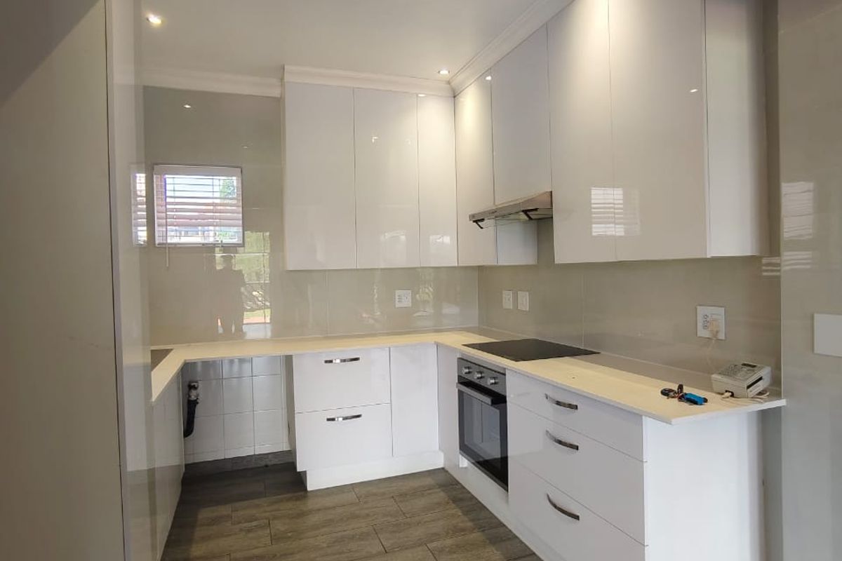 Modern kitchen featuring high-gloss white cabinetry, integrated oven, electric hob, extractor fan, and tiled flooring with a neutral backsplash.