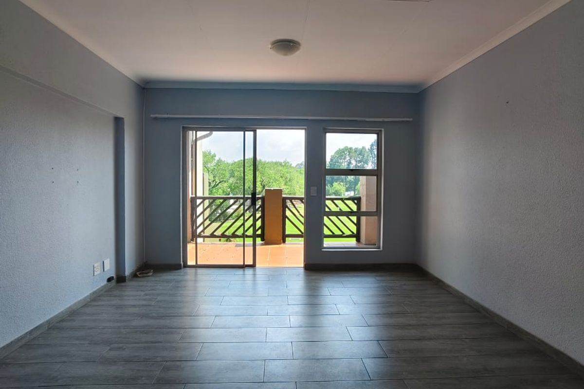 An empty living room featuring modern wood-look floor tiles, neutral walls, and a sliding glass door providing access to a private balcony.