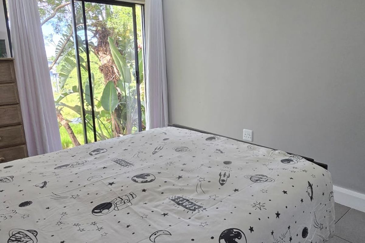 A well-maintained bedroom featuring neutral grey walls, tiled flooring, recessed downlighting, and a large sliding glass door providing natural light and garden views.