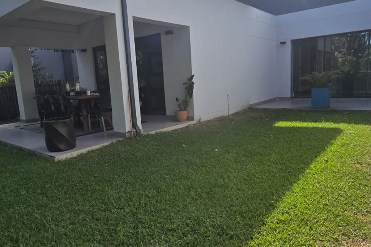 A rear view of the property featuring a covered patio area, sliding glass doors, and a well-maintained lawn.