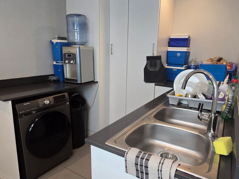 A functional laundry area featuring built-in white cabinetry, a double stainless steel sink with a modern mixer tap, and tiled flooring.