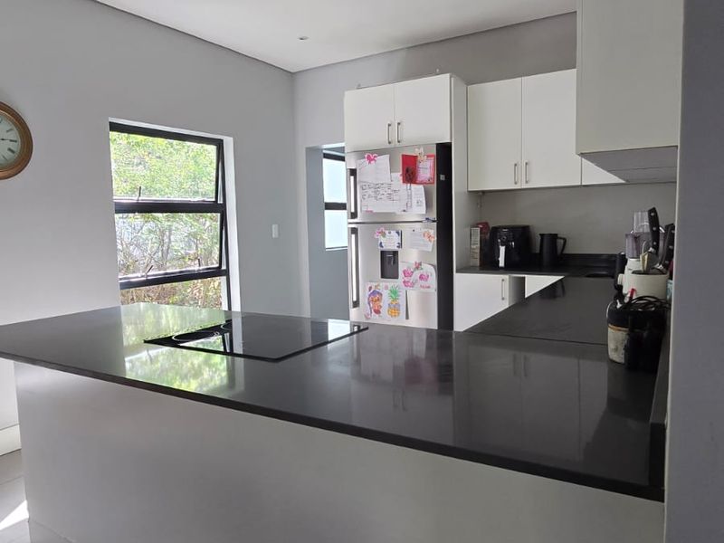 Modern kitchen featuring sleek white cabinetry, dark stone countertops, an integrated electric hob, and large format floor tiles.