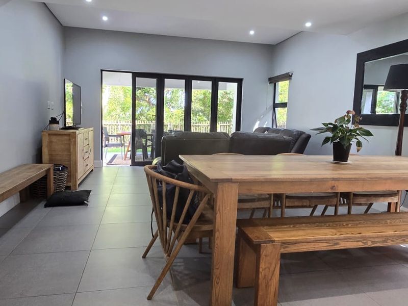 Spacious open-plan living and dining area featuring large format floor tiles, recessed downlighting, and seamless access to the outdoor patio through sliding glass doors.